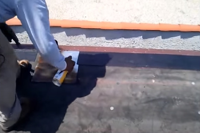 Meridian Roofing worker spraying the metal boot on ventilation of commercial flat roof